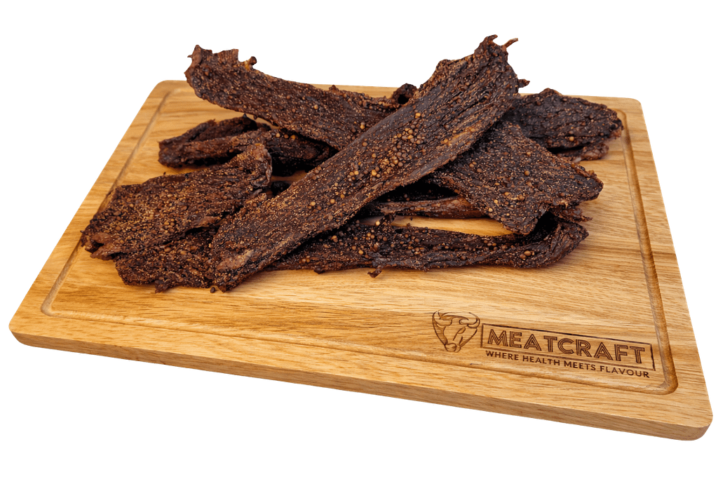 Handcrafted beef biltong with coriander seasoning on a wooden MeatCraft board, isolated on a white background
